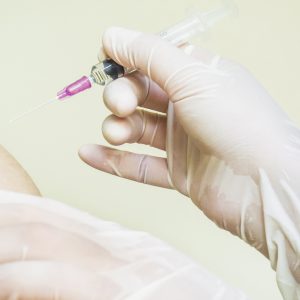 A vaccination needle approaching another person's shoulder